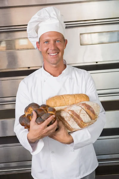 Leende baker håller färska limpor — Stockfoto