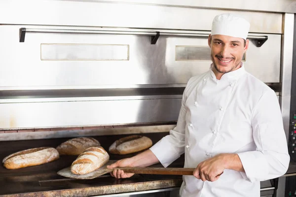Happy baker taking out fresh loaf — Stock Photo, Image