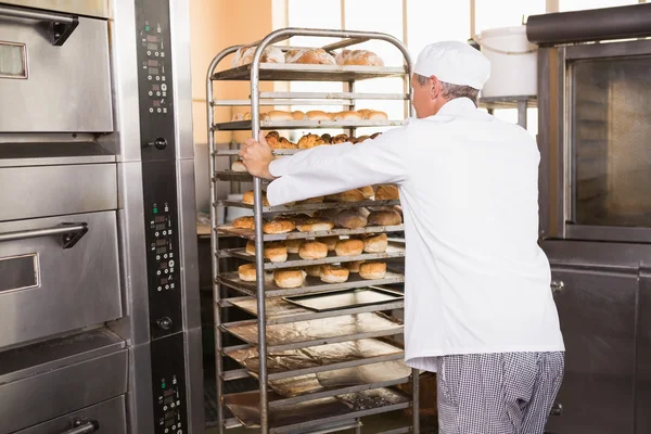 Smiling baker pushing tray of bread — Stock Photo, Image