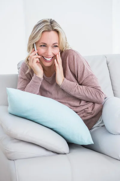Uśmiechnięta blondynka siedzi na kanapie dzwoniąc — Zdjęcie stockowe