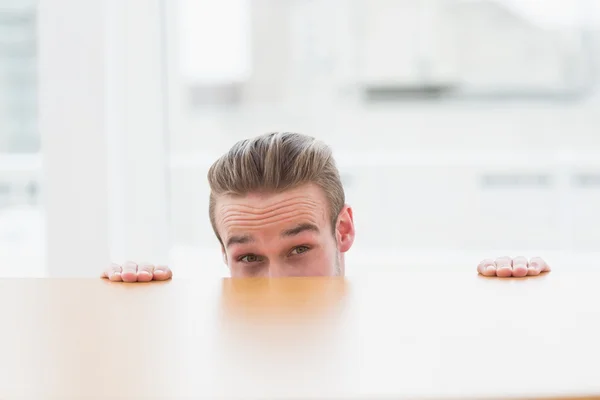 Nervous businessman peeking over desk — Stock Photo, Image