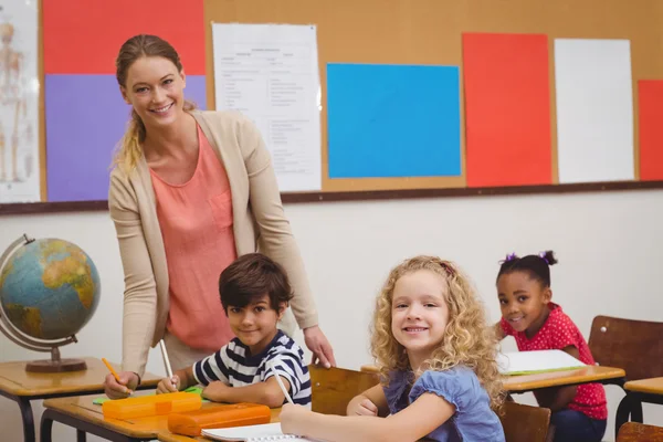 Mooie leraar helpen leerling in de klas glimlachen op camera — Stockfoto