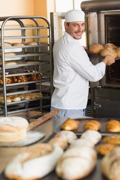 Happy baker taking out fresh loaves — Stock Photo, Image