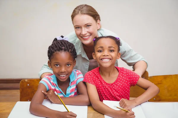 Cute pupils and teacher smiling at camera in classroom — Stock Photo, Image