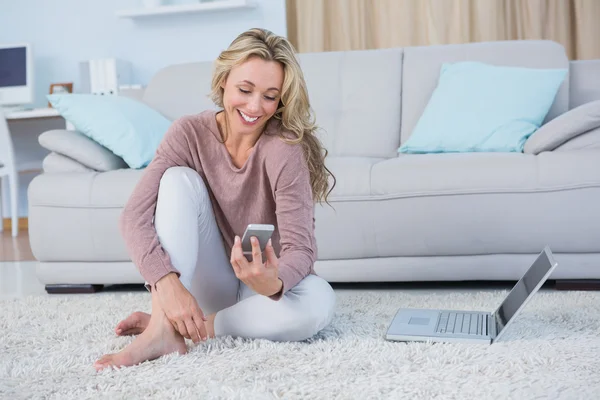 Blondine sitzt mit Smartphone auf Teppich — Stockfoto