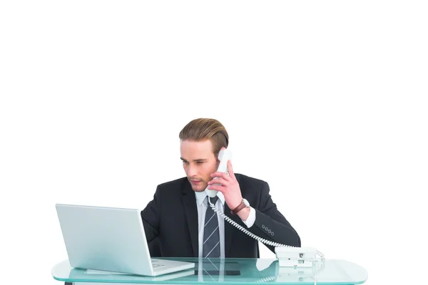 Empresário sério usando laptop enquanto telefona — Fotografia de Stock