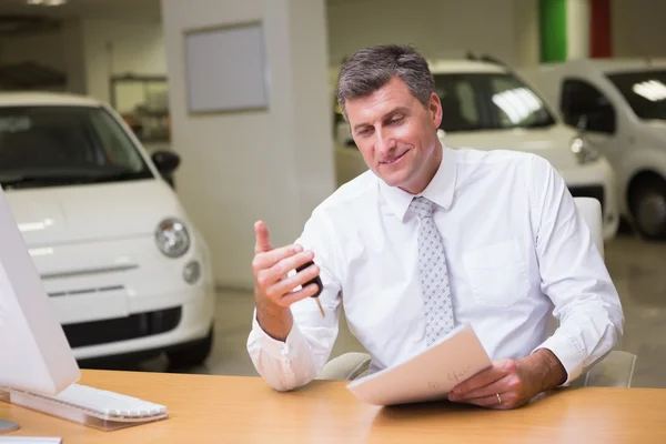 Lachende verkoper holding auto sleutel en een document — Stockfoto