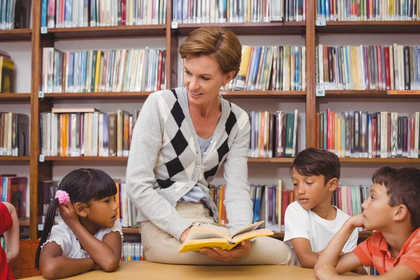 Schattig leerlingen en leraar lezen in bibliotheek — Stockfoto