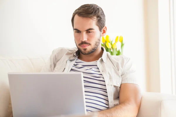 Hipster hombre usando el ordenador portátil en el sofá —  Fotos de Stock