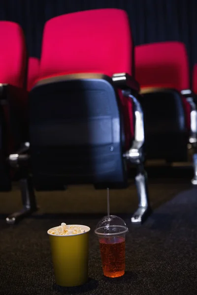 Fileiras vazias de assentos vermelhos com milho pop e bebida no chão — Fotografia de Stock
