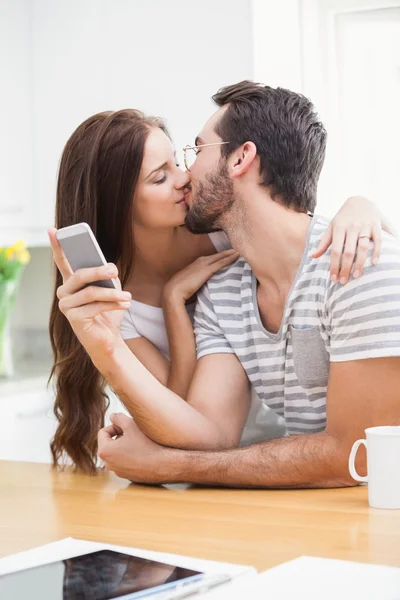 Man använder smartphone medan flickvän kysser honom — Stockfoto