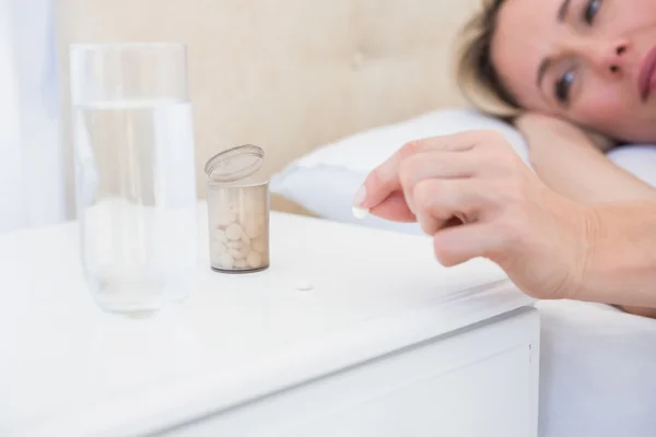 Rubia en la cama tomando pastillas en la mesita de noche — Foto de Stock