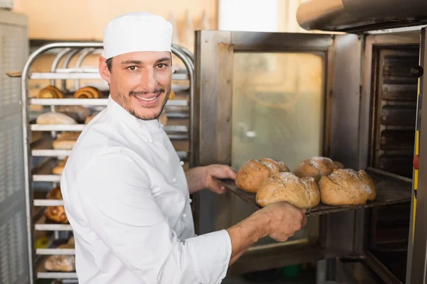 Happy baker taking out fresh loaves — Stock Photo, Image