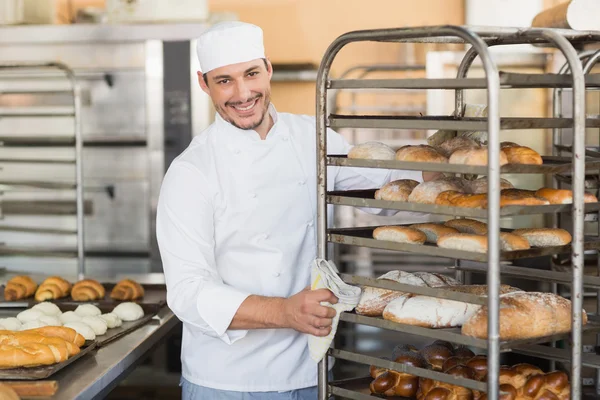 Smiling baker pushing tray of bread — Stock Photo, Image