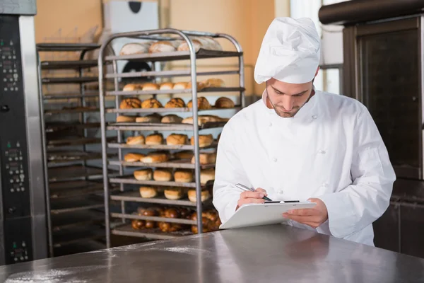 Focused baker writing on clipboard — Stock Photo, Image