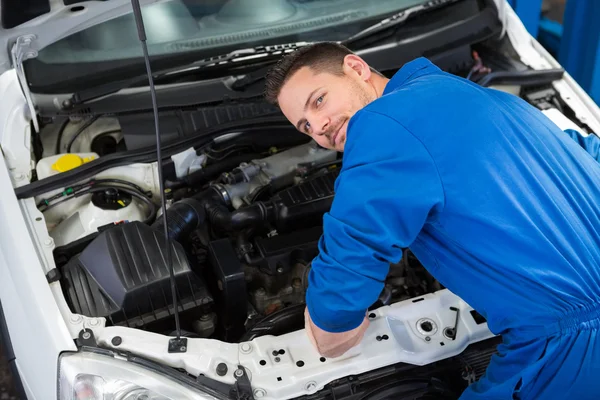 Mechanic smiling at the camera fixing engine Stock Picture