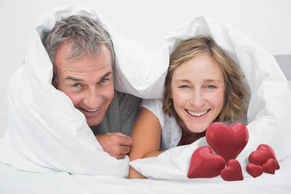 Paar unter der Bettdecke gegen Liebesherzen — Stockfoto