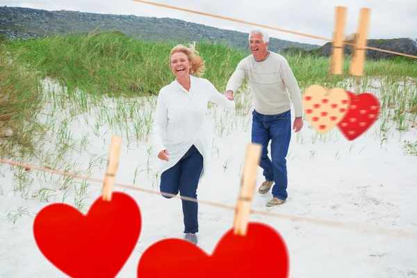 Couple sénior courant à la plage contre les cœurs — Photo