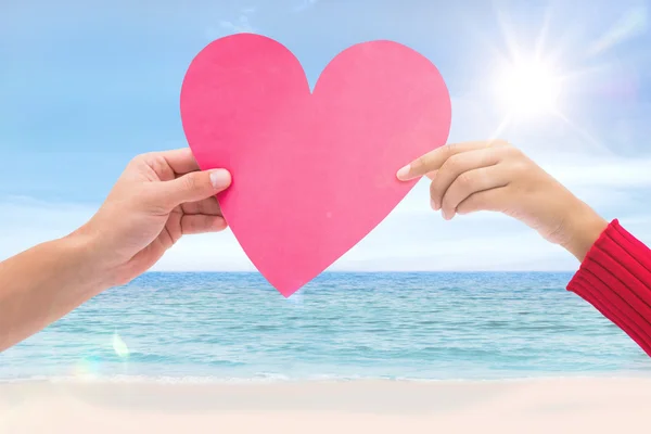 Pareja sosteniendo un corazón contra la escena de la playa — Foto de Stock