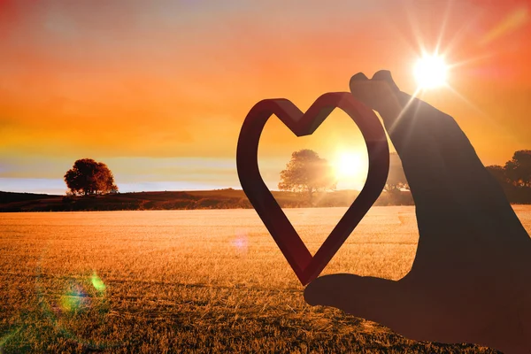 Hand presenting heart against countryside scene — Stock Photo, Image