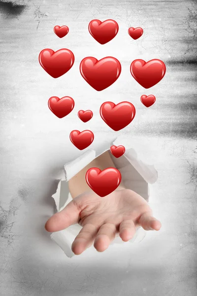 Hand bursting through paper against hearts — Stock Photo, Image