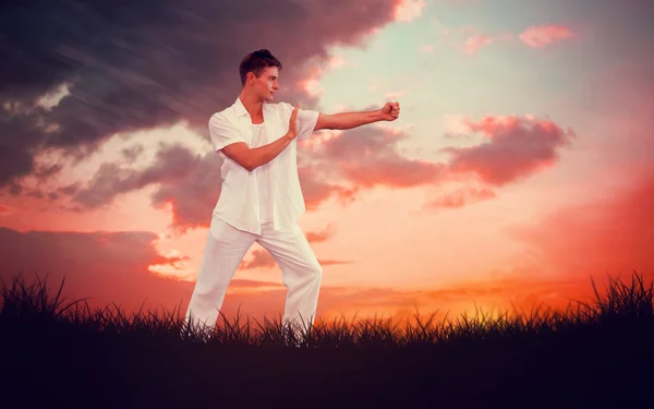 Uomo in bianco che fa tai chi contro il cielo rosso — Foto Stock