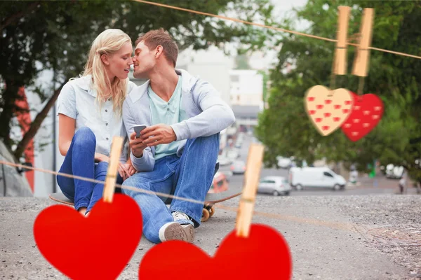 Couple sitting on skateboard kissing against hearts — Stock Photo, Image