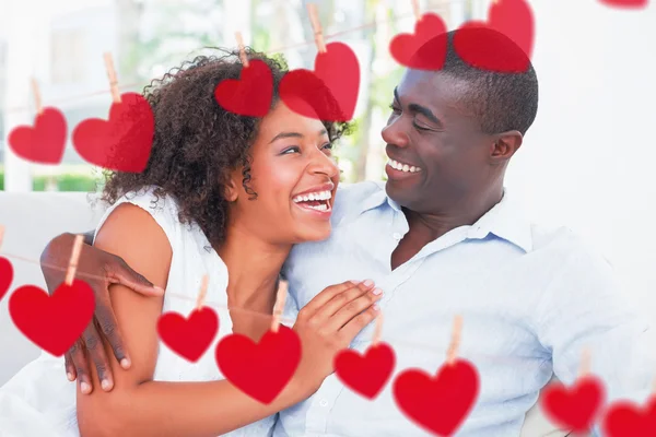 Couple cuddling on the couch against hearts — Stock Photo, Image