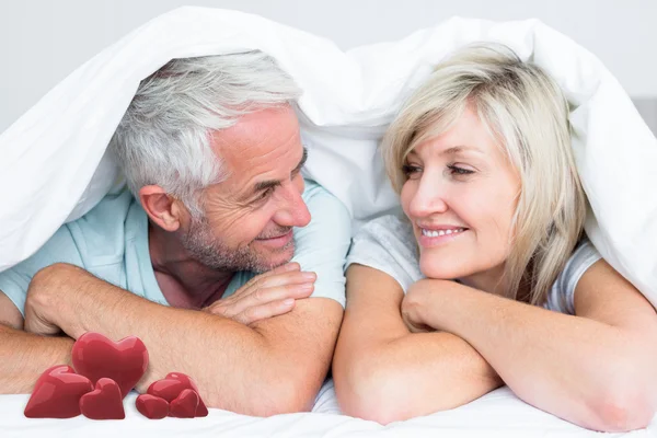 Couple lying in bed against love hearts — Stock Photo, Image