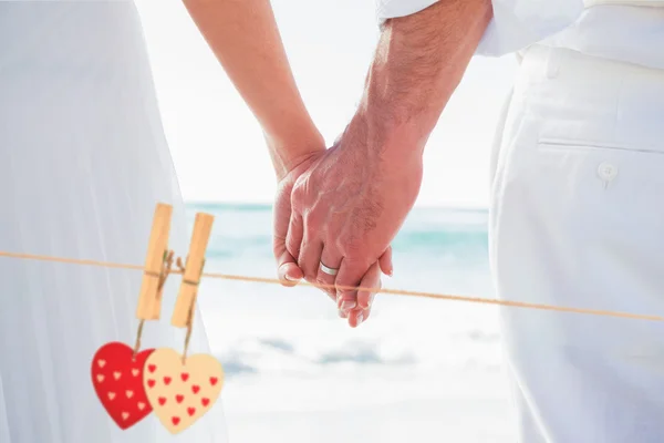 Bride and groom holding hands against hearts — Stock Photo, Image