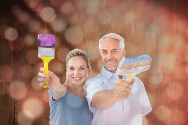 Couple holding paintbrushes smiling at camera — Stock Photo, Image