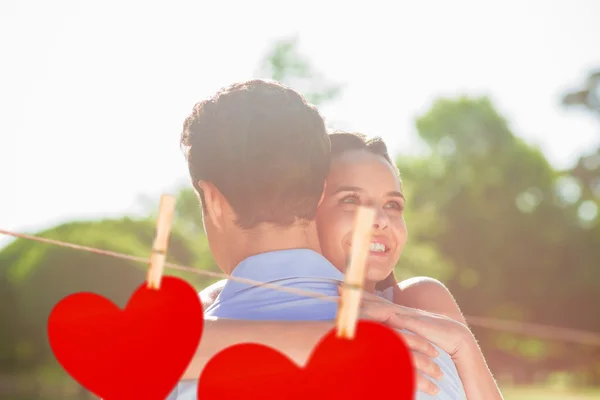 Woman embracing man at park against hearts — Stock Photo, Image
