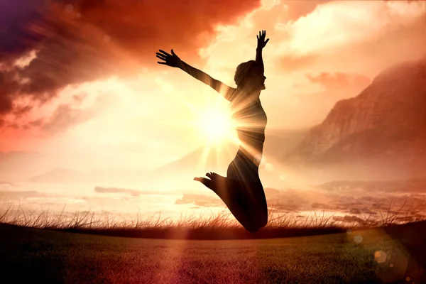 Woman jumping with arms out against sunrise — Stock Photo, Image