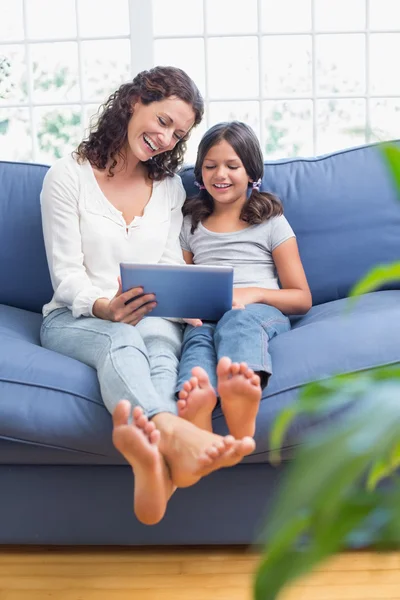 Feliz madre e hija sentadas en el sofá y usando la tableta —  Fotos de Stock