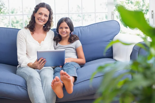 Lycklig mor och dotter sitter i soffan och använder tablet — Stockfoto