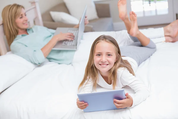 Mère utilisant un ordinateur portable tandis que la fille utilisant tablette PC sur le lit — Photo