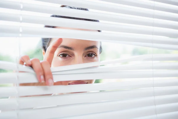 Frau blickt durch Jalousien — Stockfoto