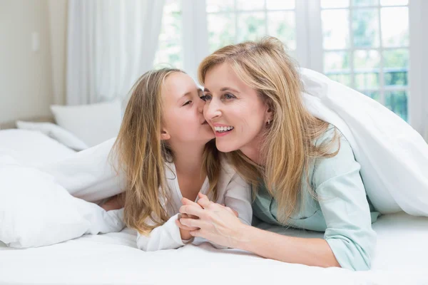 Filha beijando sua mãe na bochecha na cama — Fotografia de Stock