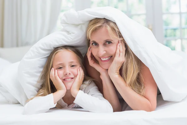 Moeder en dochter kijken camera onder het dekbed — Stockfoto