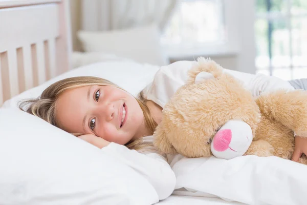 Kleines Mädchen liegt in ihrem Bett und hält ihren Teddy — Stockfoto