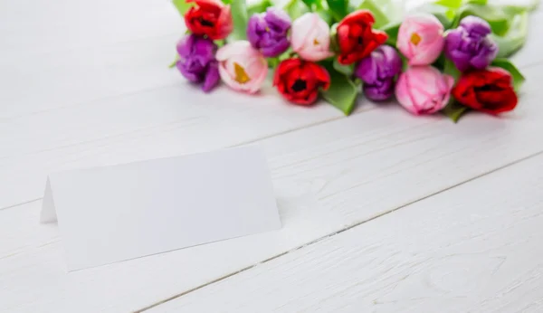 Tulpen en witte kaart op houten tafel — Stockfoto