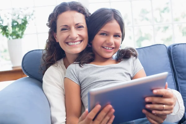 Lycklig mor och dotter sitter i soffan och använder tablet — Stockfoto