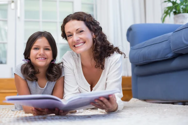 Feliz madre e hija tumbadas en el suelo y leyendo un libro —  Fotos de Stock