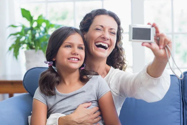 Happy mother and daughter sitting on the couch and taking selfie — Stock Photo, Image