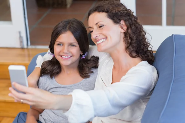 Feliz madre e hija sentadas en el sofá y tomando selfie —  Fotos de Stock