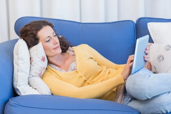 Brunette couchée sur le canapé et utilisant une tablette — Photo