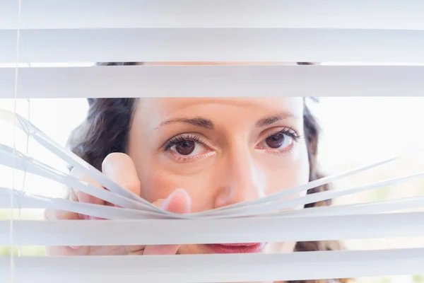 Femme curieuse regardant à travers les stores — Photo