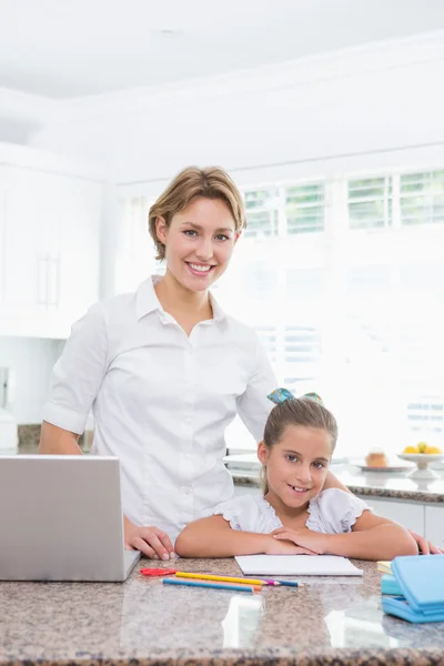 Little girl doing her homework with mother using laptop — Stock Photo, Image
