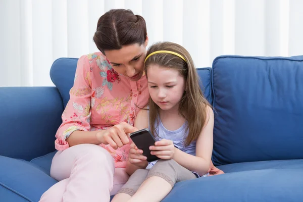 Madre e hija usando teléfono inteligente en el sofá —  Fotos de Stock