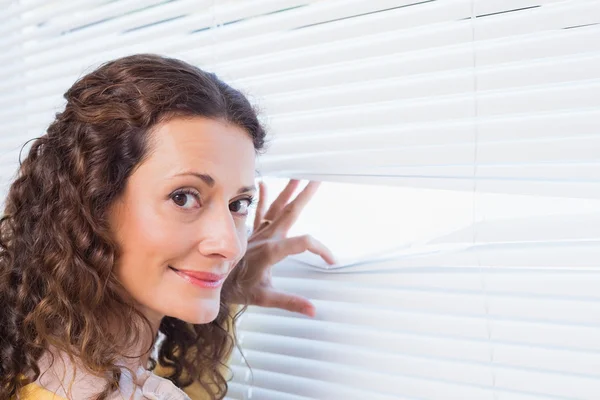 Nieuwsgierig vrouw op zoek via blinds — Stockfoto